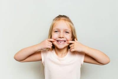 young girl smiling and pointing at teeth with a big grin